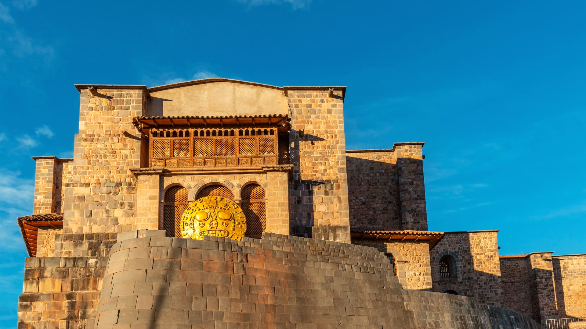 Muro inca curvo del Qorikancha con un sol dorado bajo cielo azul