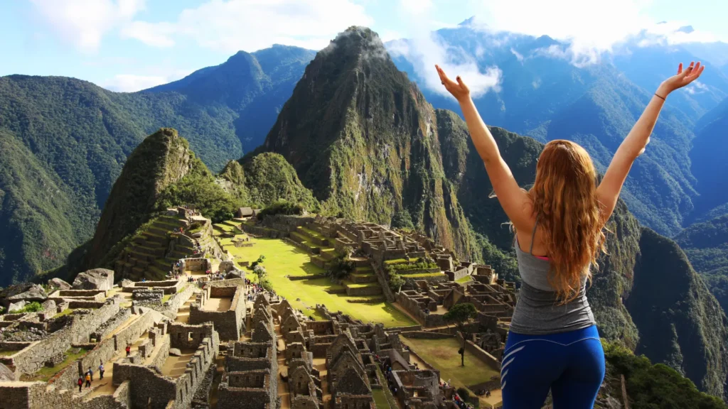 Mujer con los brazos en alto frente a Machu Picchu y la montaña Huayna Picchu