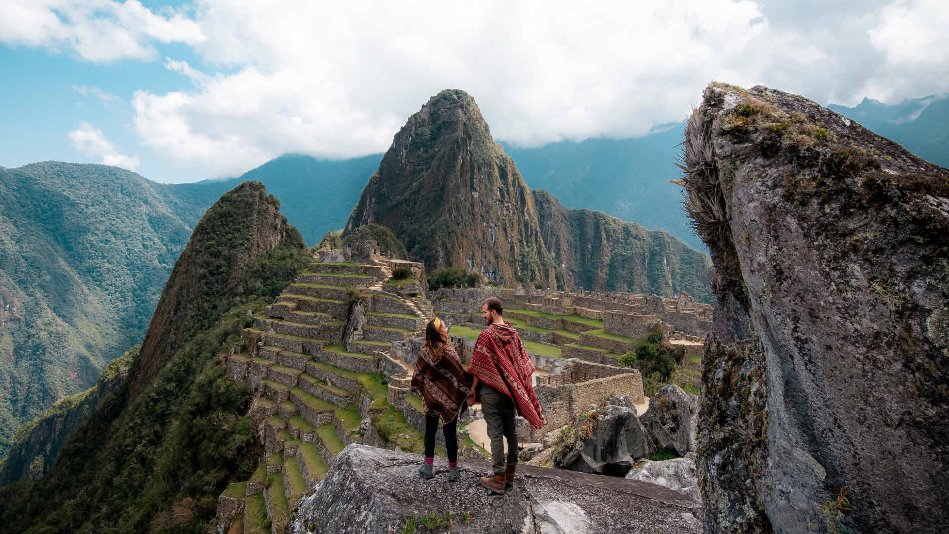 Pareja con ponchos andinos tomada de la mano sobre Machu Picchu