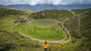 Mujer con casaca amarilla frente a los andenes circulares incas de Moray
