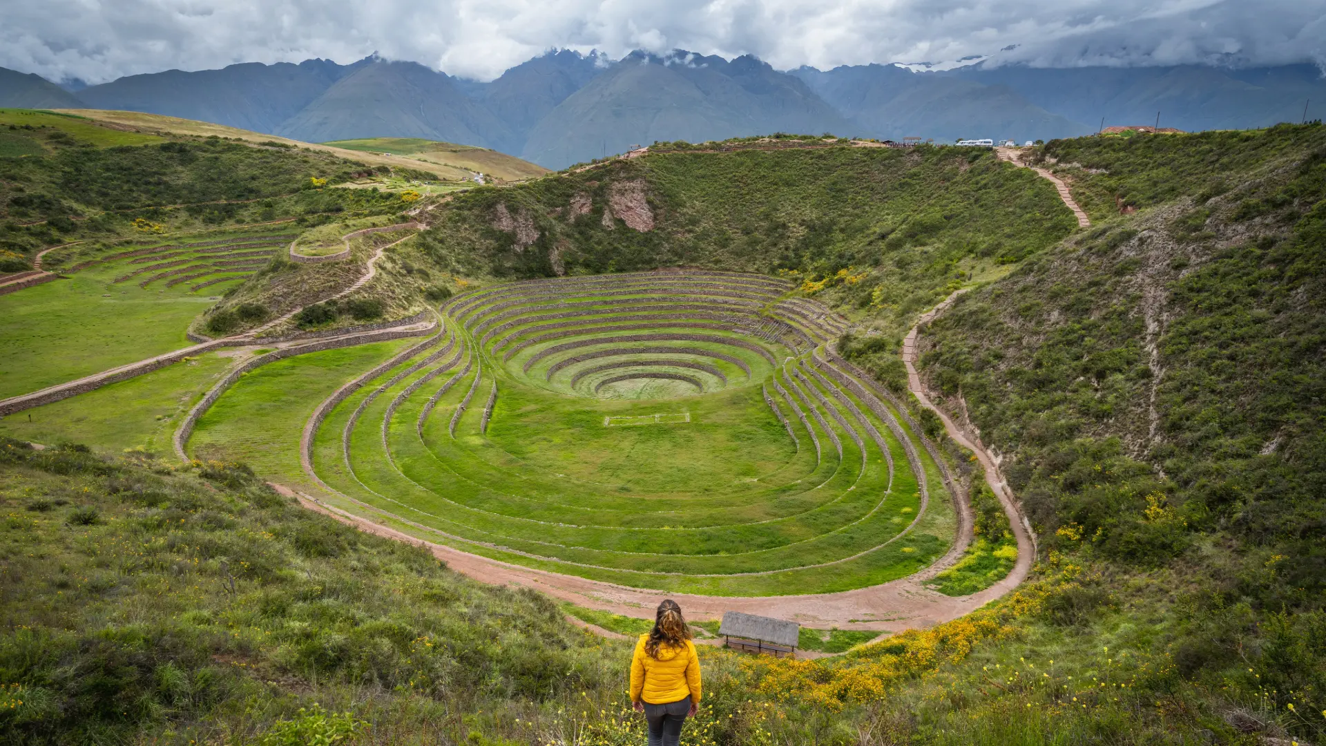Mujer con casaca amarilla frente a los andenes circulares incas de Moray