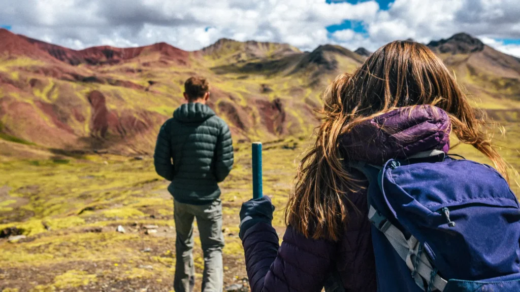 Casal caminhando por um vale de morros avermelhados a caminho da Montanha Colorida