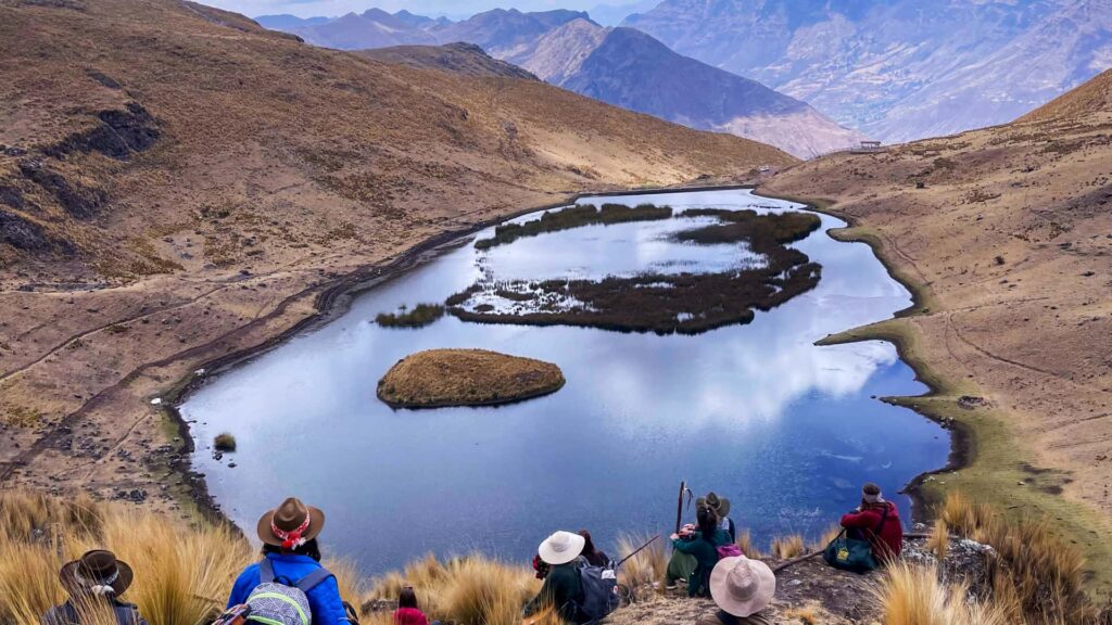Hikers in hats resting above a highland lagoon in an Andean valley