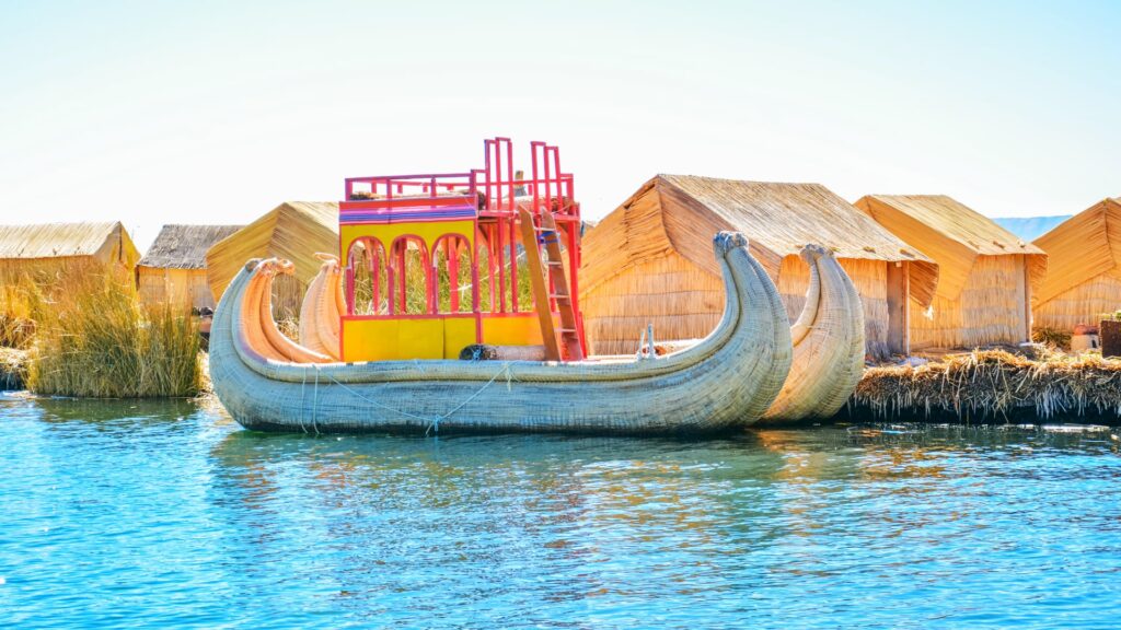 Totora reed boat beside reed houses on the Uros floating islands, Lake Titicaca
