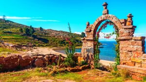 Arco de pedra com flores diante de uma praia do lago Titicaca